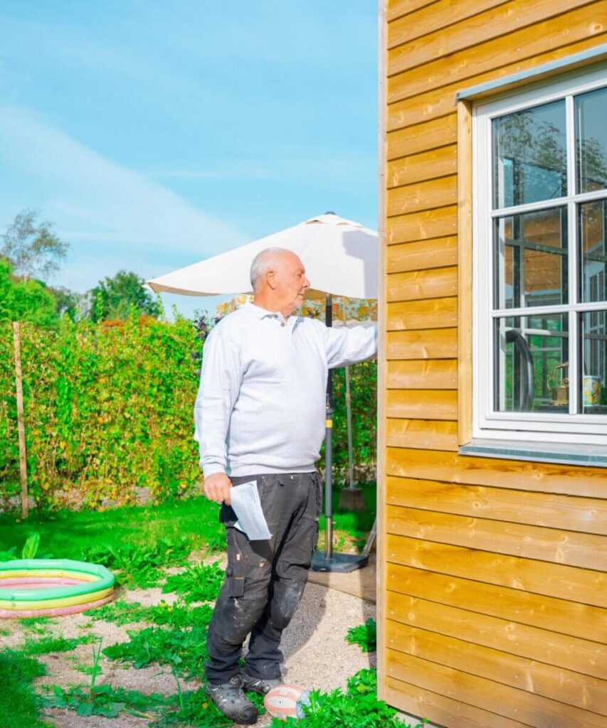 Ældre tømrer i have med hus i træ