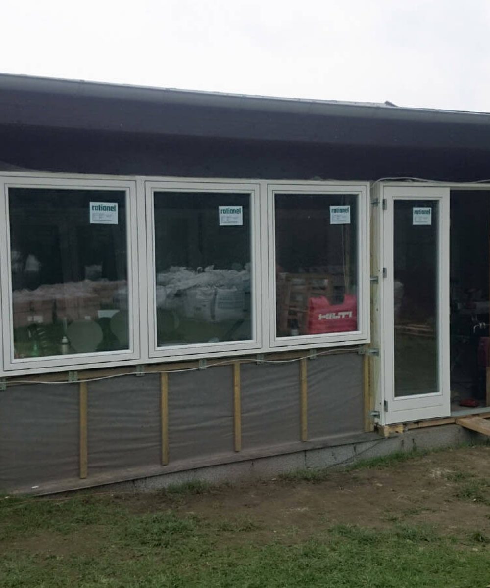 Igangværende nybyg af hus med hvide vinduer. Græs foran hus